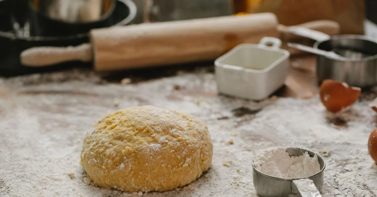 Pâte saupoudrée de farine avec un rouleau à pâtisserie et des ustensiles de cuisine sur une surface en bois dans une cuisine familiale.
