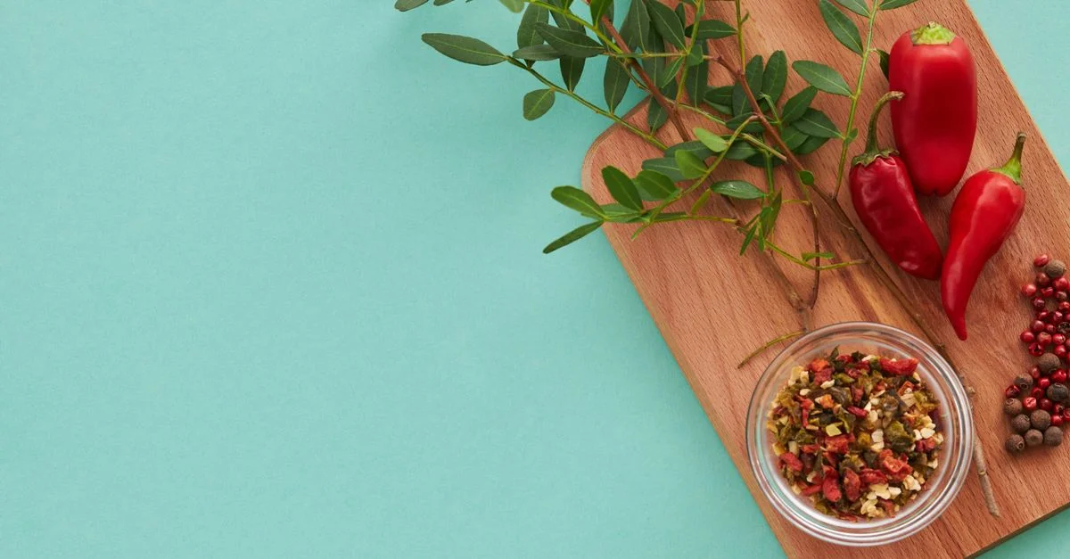 Frais feuilles vertes et poivrons rouges sur une planche à découper avec un bol d'épices. Parfait pour l'inspiration culinaire.