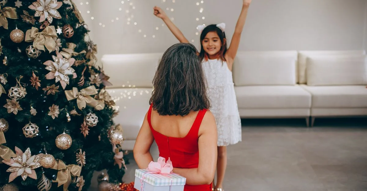 Un moment joyeux pendant les fêtes alors qu'une mère surprend sa fille avec un cadeau de Noël près d'un sapin décoré.