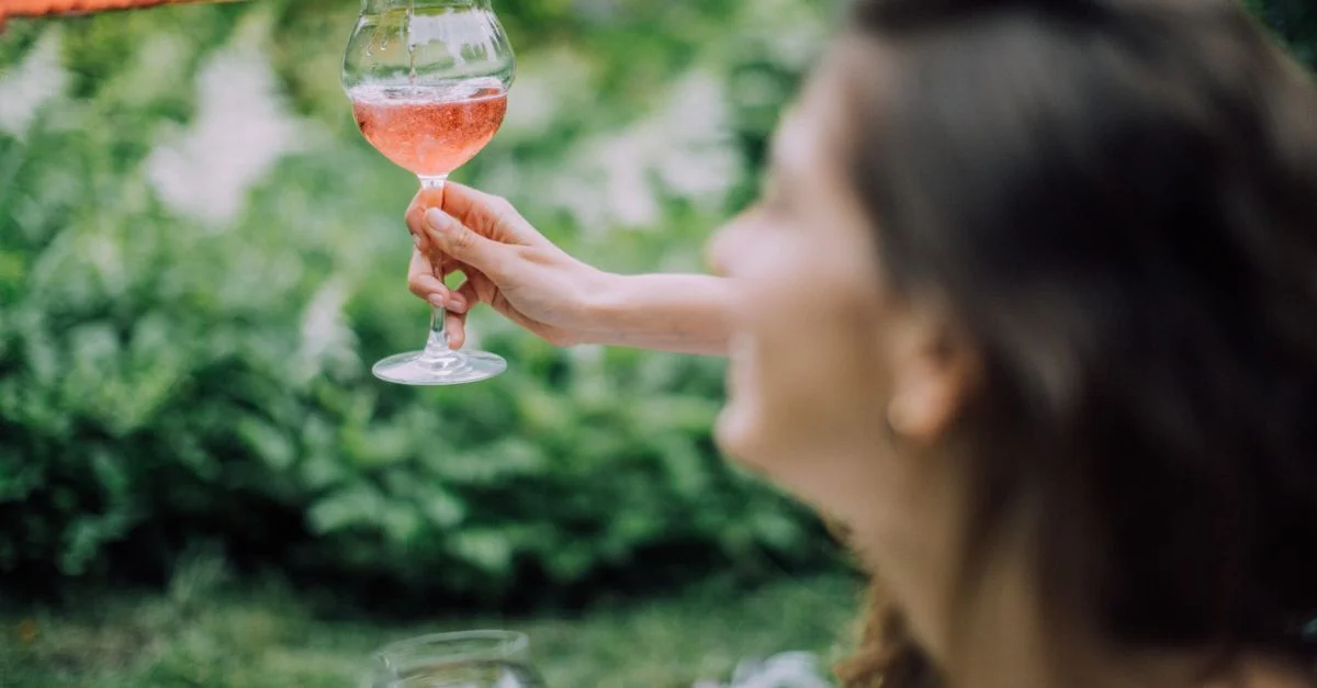 Une femme verse élégamment du vin rosé dans un verre lors d'un pique-nique en plein air ensoleillé, capturant une ambiance estivale détendue.