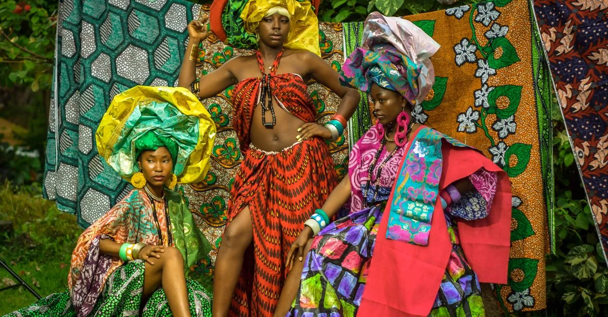 Un portrait coloré de trois femmes en tenue traditionnelle africaine mettant en valeur des tissus aux couleurs chatoyantes.