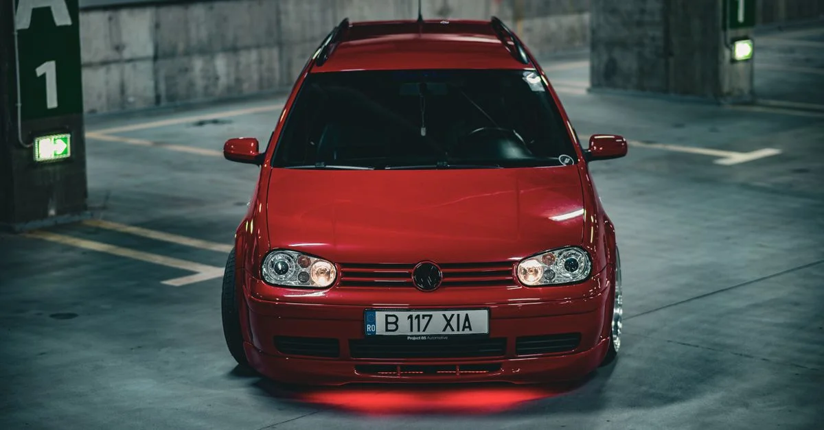 Une voiture rouge éclatante est garée dans un garage souterrain faiblement éclairé, l'accent étant mis sur sa couleur vive et son design élégant.