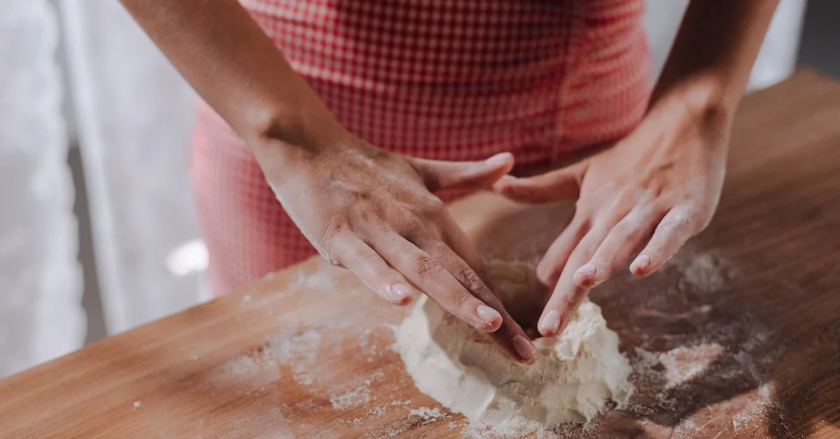 Gros plan d'une femme façonnant de la pâte à pâtes fraîche sur une surface en bois.