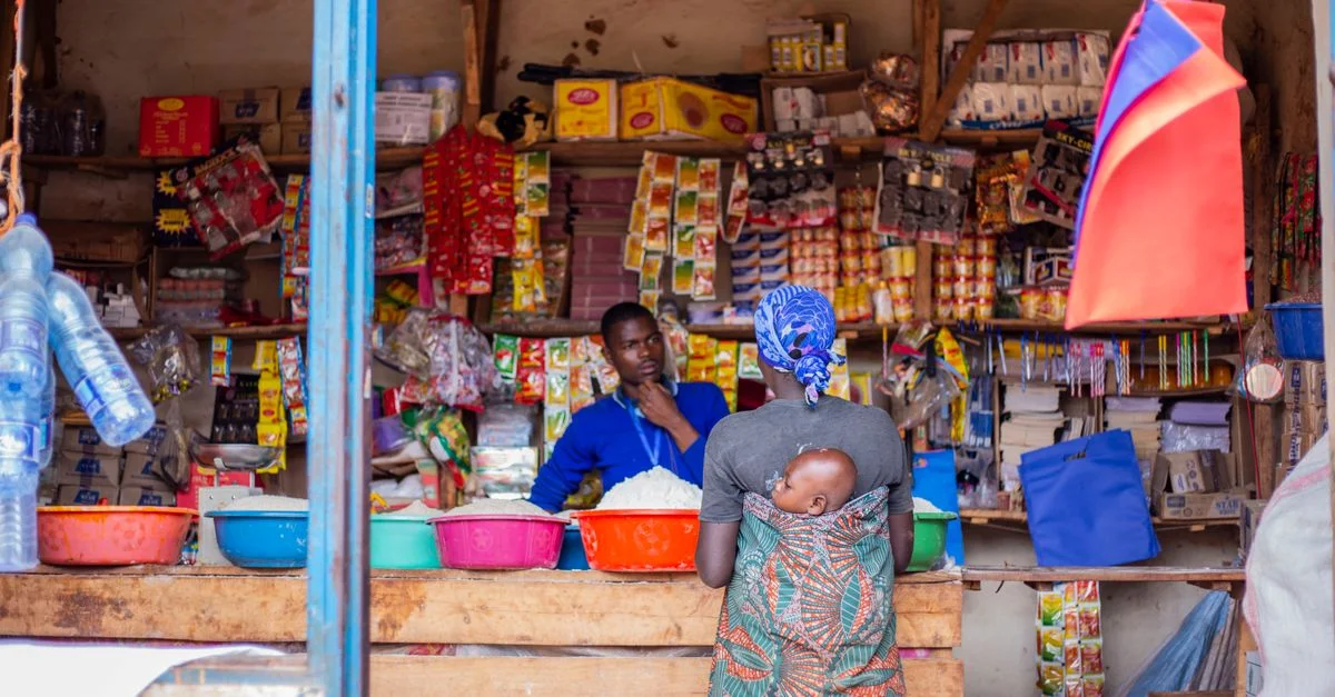 Une femme avec un bébé en écharpe fait ses courses dans un stand de marché traditionnel vibrant.